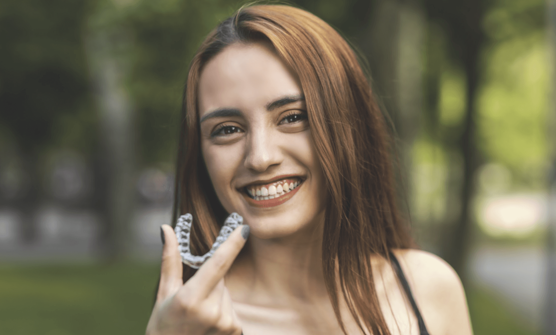 Lady smiling and holding Invisalign clear aligners at Sparkling Dental