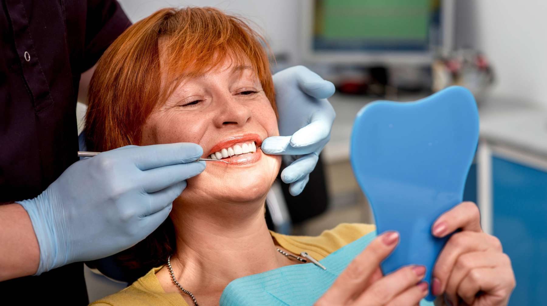 Lady looking at her teeth in the mirror after cracked tooth repair at Sparkling Dental